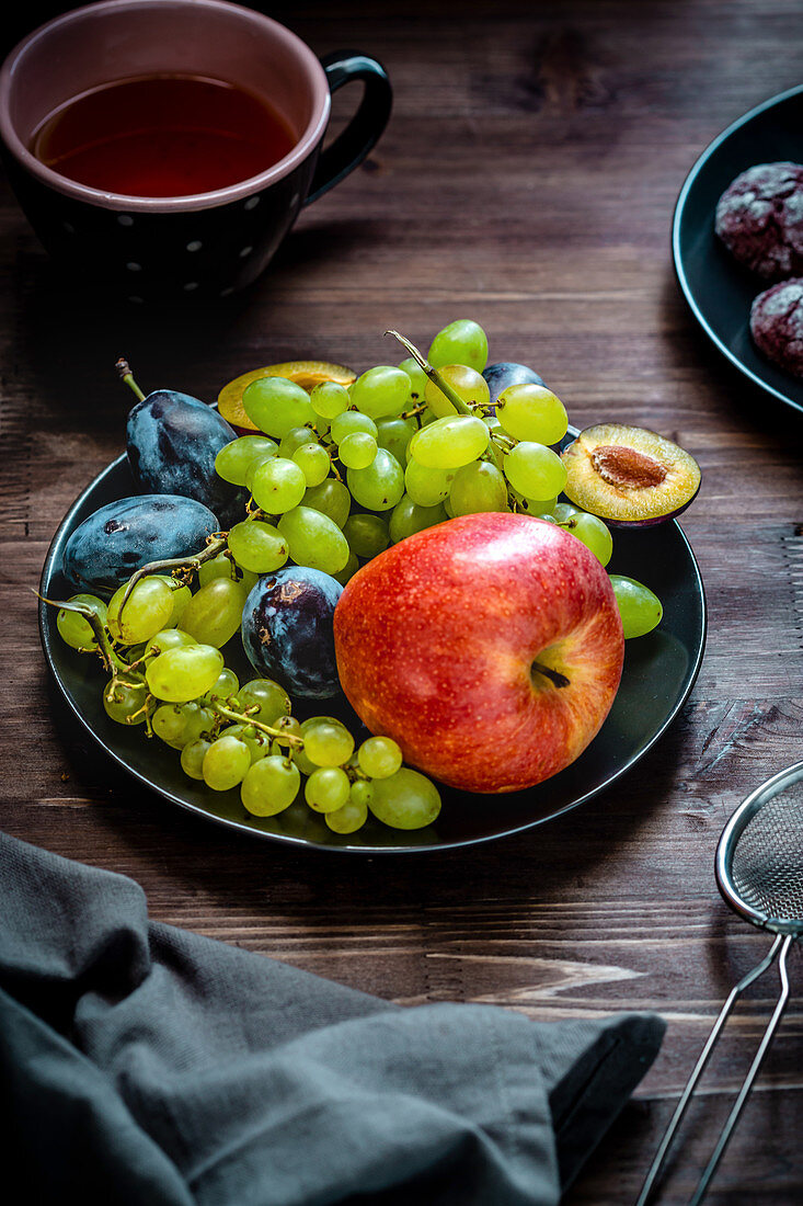 Teller mit Früchten - Apfel, weiße Trauben und Pflaumen