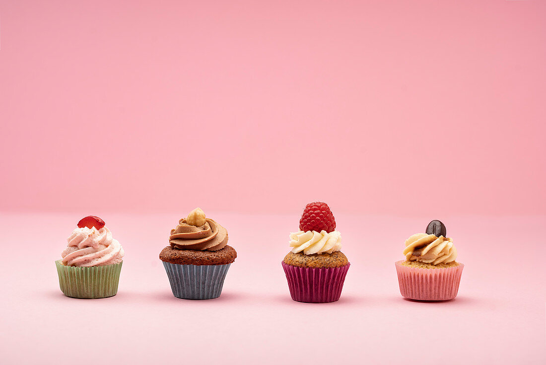 Verschiedene Mini-Cupcakes vor rosafarbenem Hintergrund