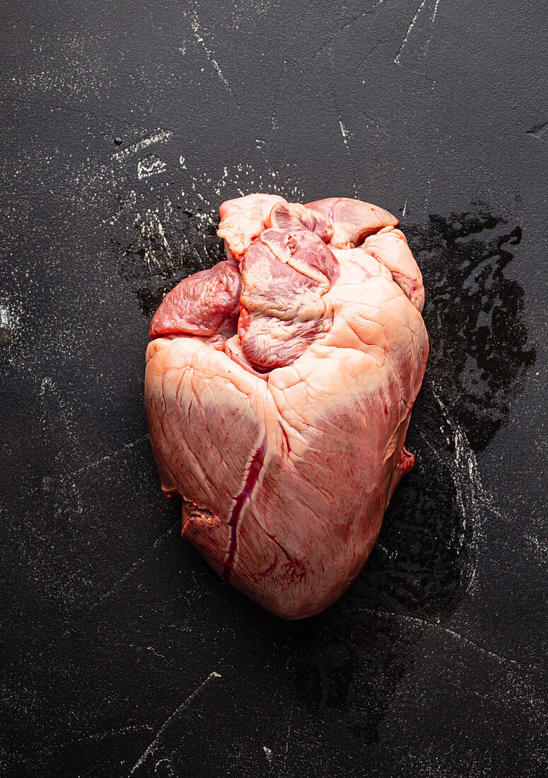 Raw whole beef heart on black stone background