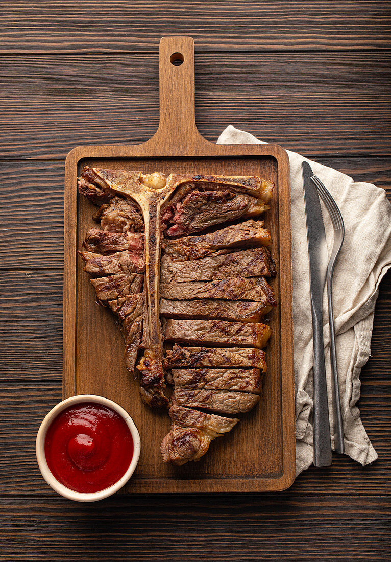 Sliced grilled medium rare T-bone beef steak with ketchup
