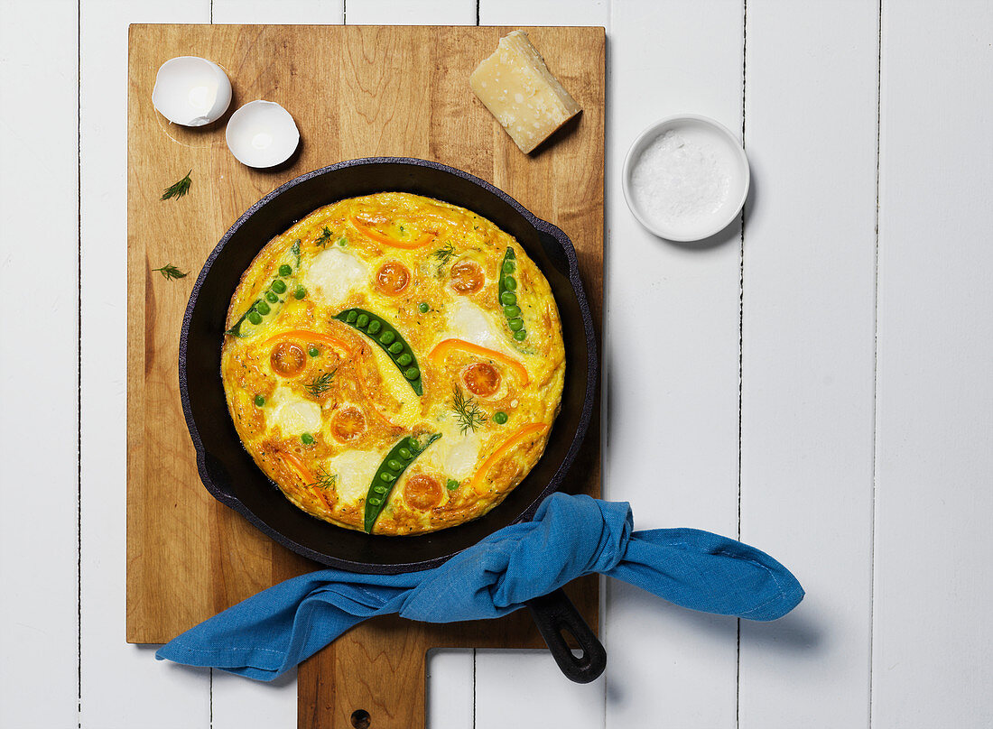 Frittata mit Tomaten, Erbsen und Käse in einer Gusseisenpfanne auf Holzschneidebrett