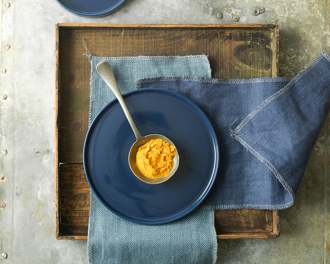Overhead View of Tumeric Spice in Antique Spoon on Blue Plate