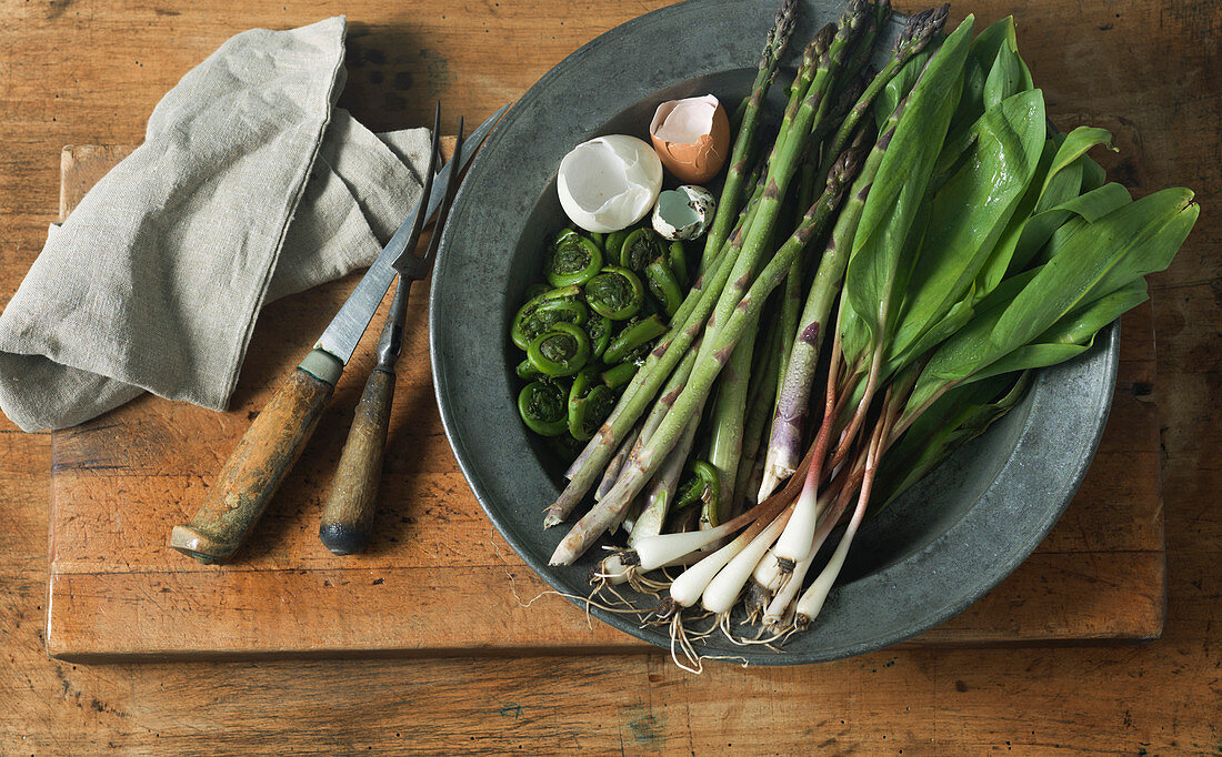 Overhead View of Asparagus, Fiddleheads, Ramps And Egg Shells on Pewter Plate With Cutlery and Napkin