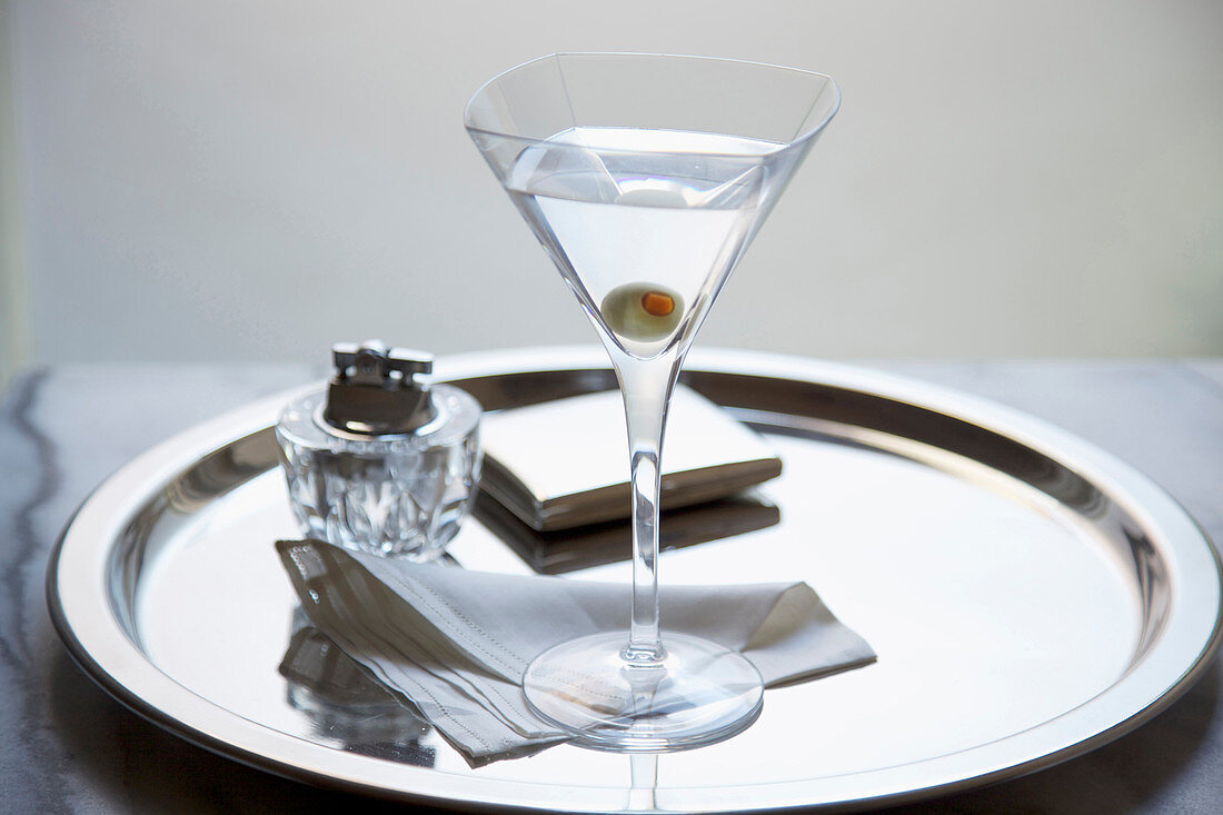 Martini mit grüner Olive auf silbernem Tablett, Zigarettenetui und Cocktailserviette