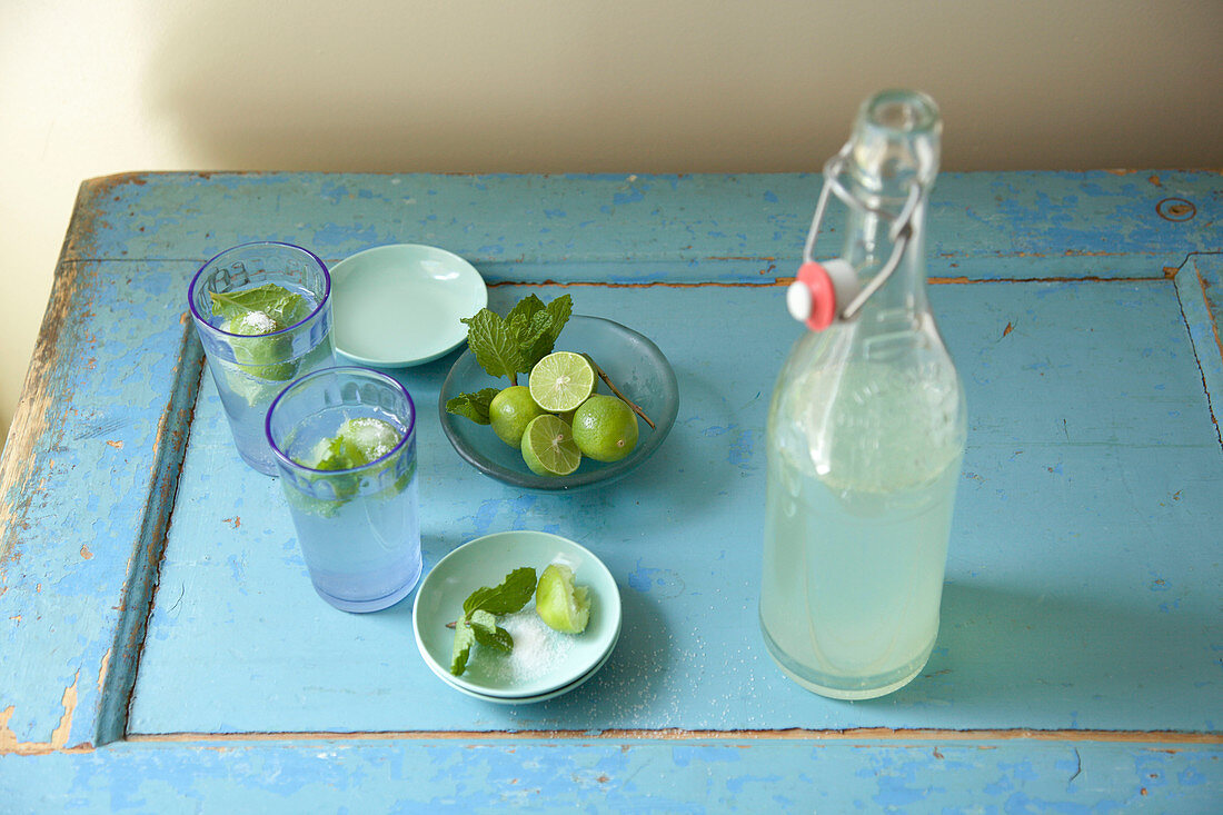 Mojito in zwei Gläsern, Schälchen mit Limetten, Minze und Zucker