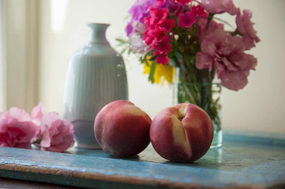 Pfirsiche auf einem Tablett mit Vasen und frischen Blumen