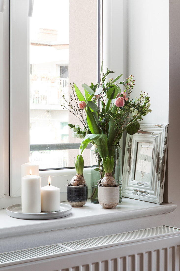 Spring bouquet of tulips and white candles on windowsill