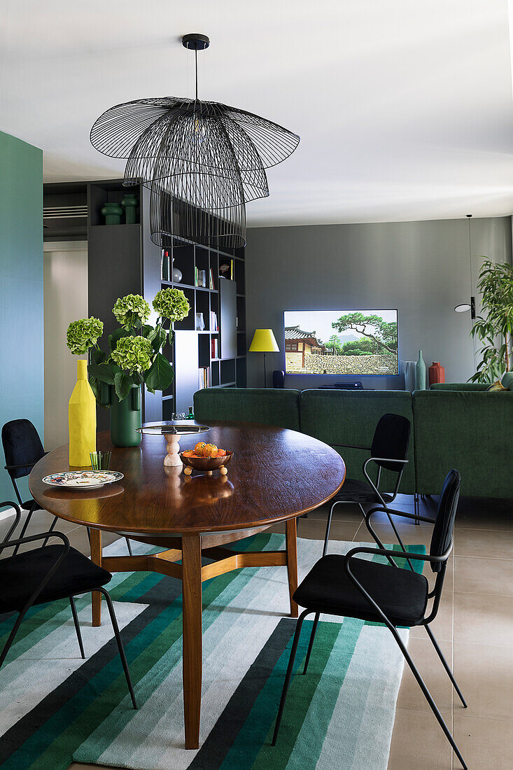 Oval dining table surmounted by black metal hanging pendant lamp in open plan living space