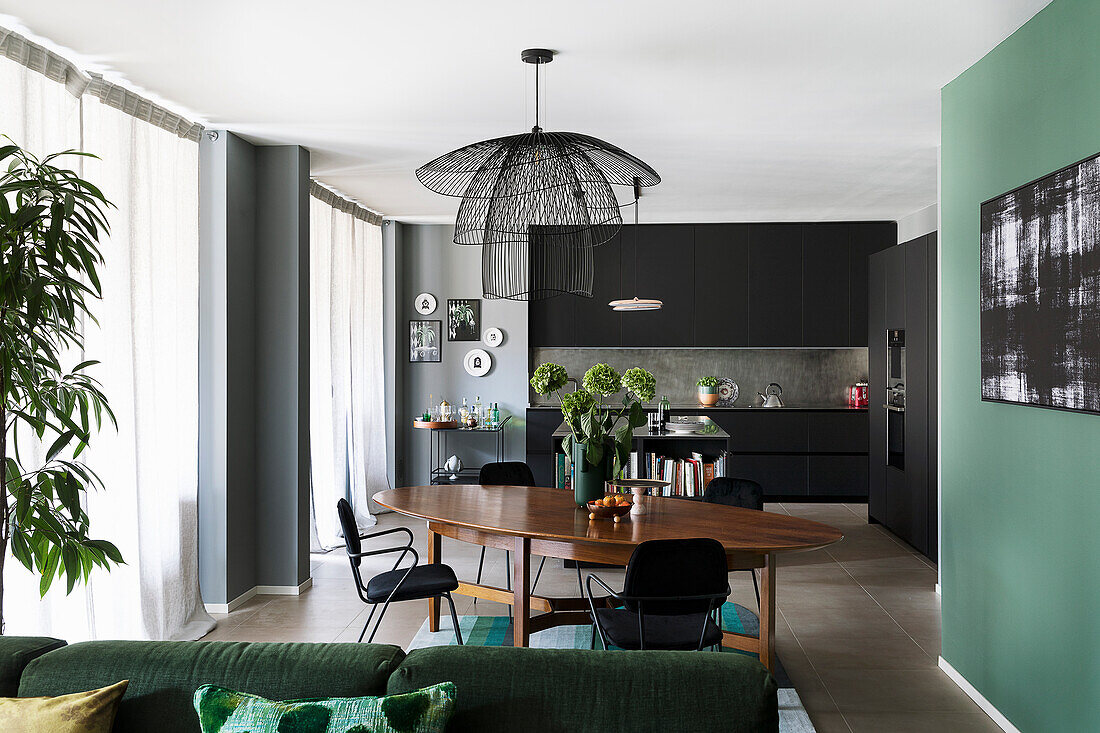 Offener Wohnraum mit schwarzer Einbauküche, Essbereich und grünem Sofa
