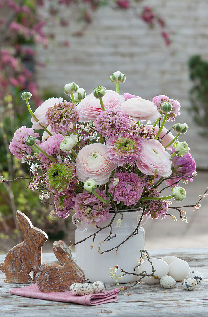 Pastel-colored Easter bouquet with ranunculus and Sea lavender, wooden Easter bunnies, and Easter eggs