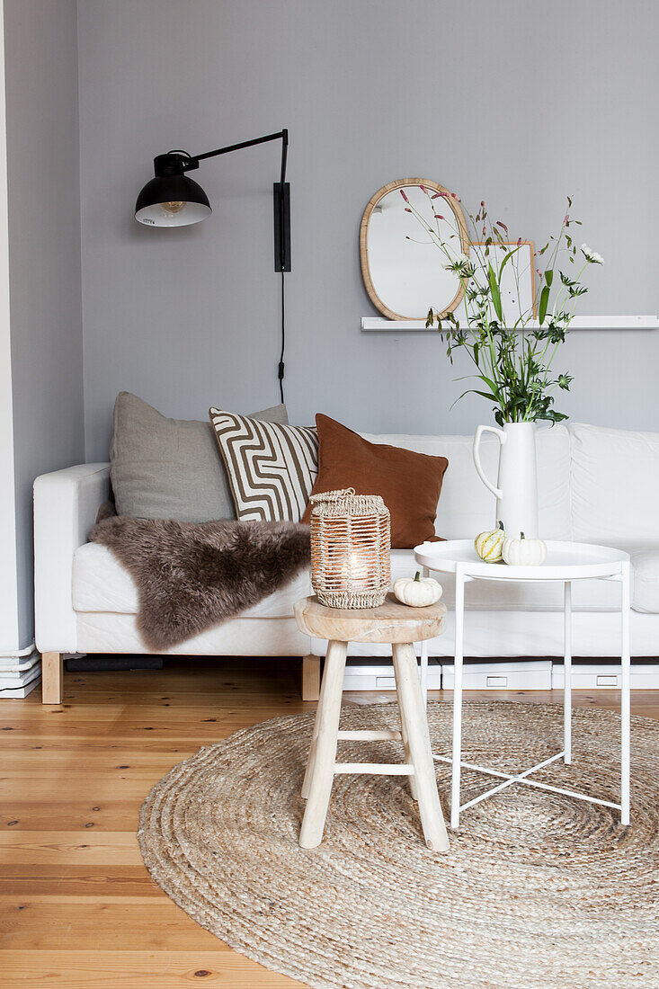 White sofa with scatter cushions, white side table with jug vase and wooden stool with lantern in living room