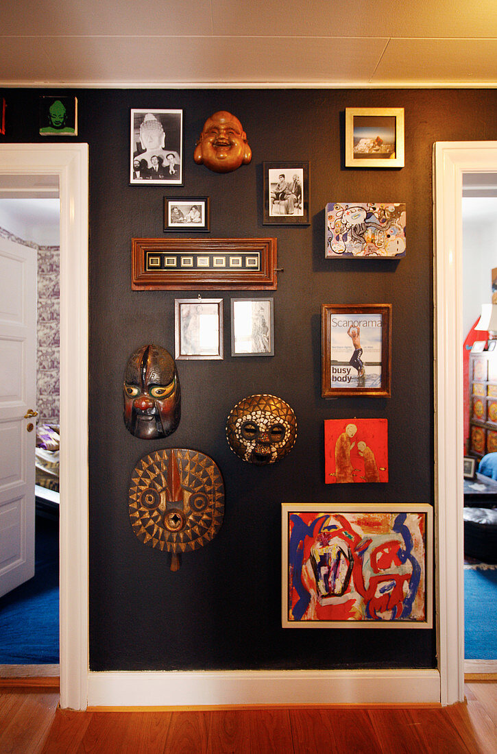 Masks, mirrors, paintings and photos on black wall in hallway
