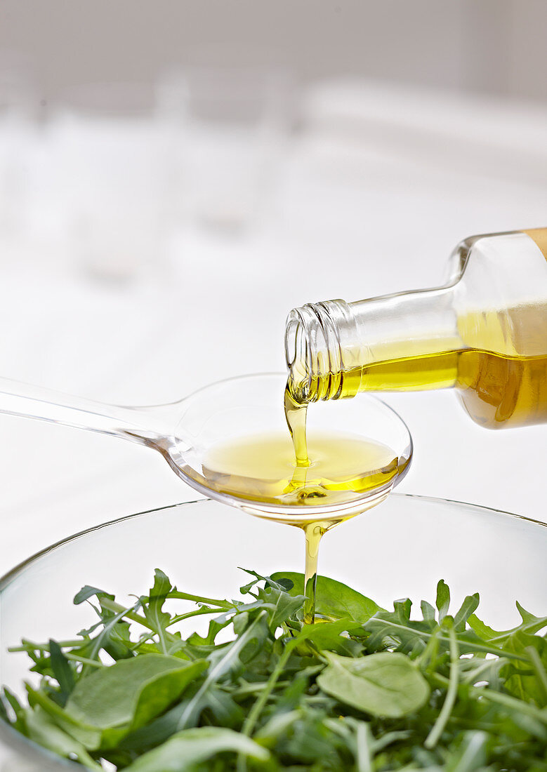 Olivenöl auf Löffel über grünem Salat