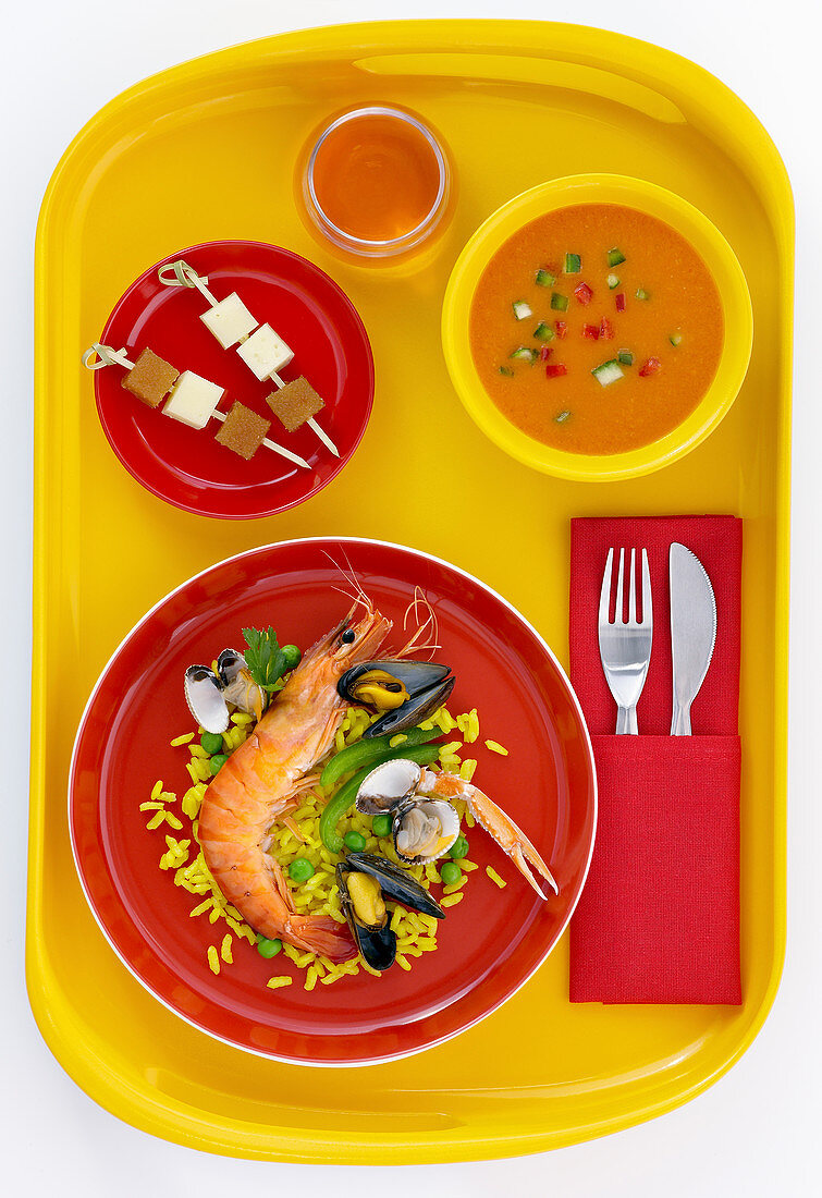 Spanisches Menü mit Gazpacho, Paella und Käsespießen auf gelbem Tablett