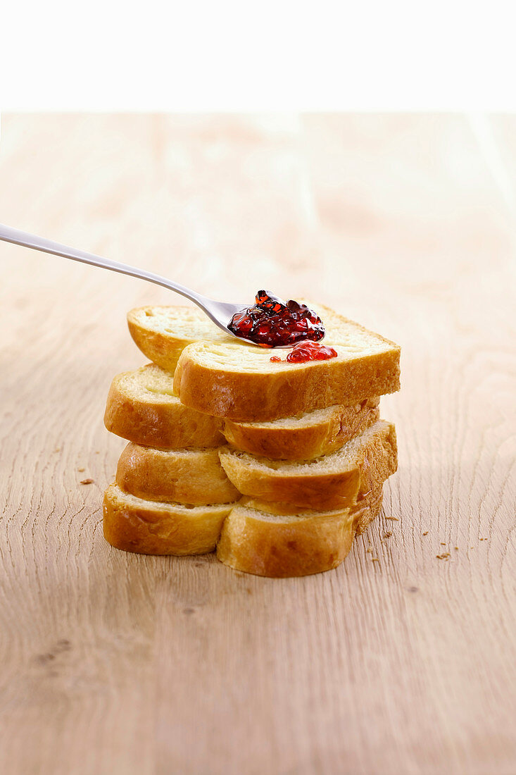 Spoon of red jam on pile of sliced brioche