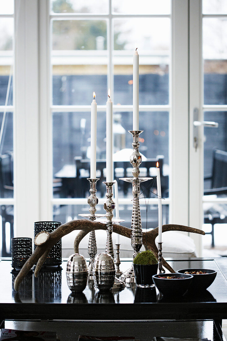 Silberne Kerzenständer mit weißen Kerzen und Geweih auf schwarzem Tisch