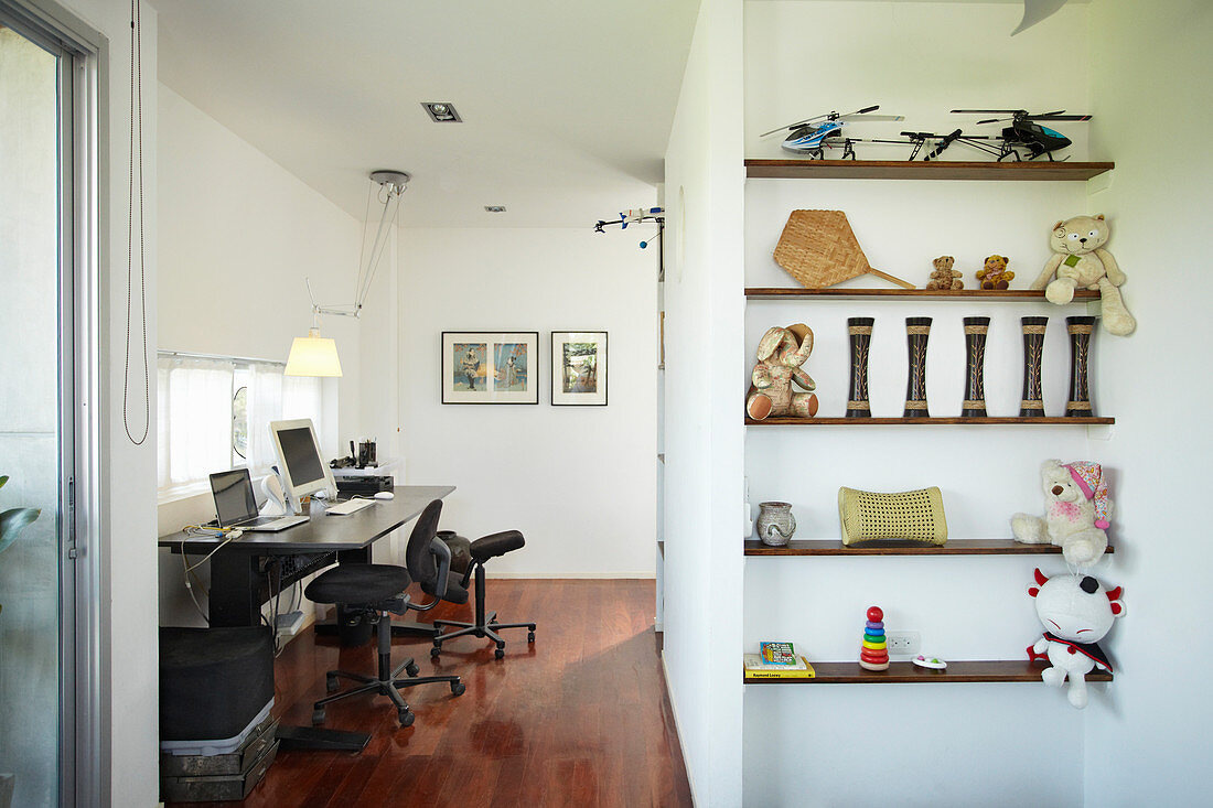 View into study with black desk; childhood mementoes on shelves in foreground