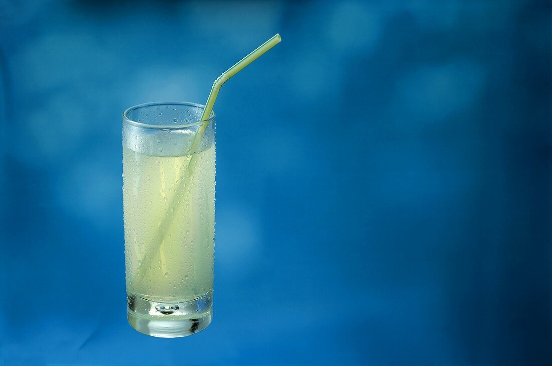 Lemonade in glass with straw against blue background