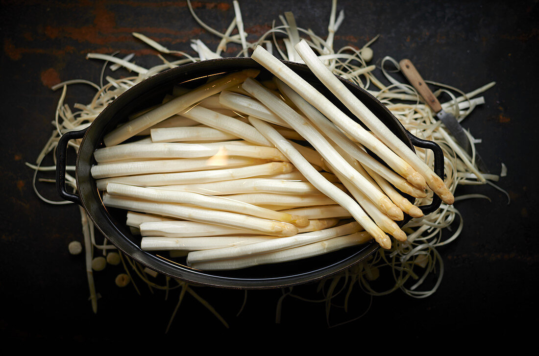 Geschälter Spargel im Topf drumherum Spargelschalen und Schälmesser