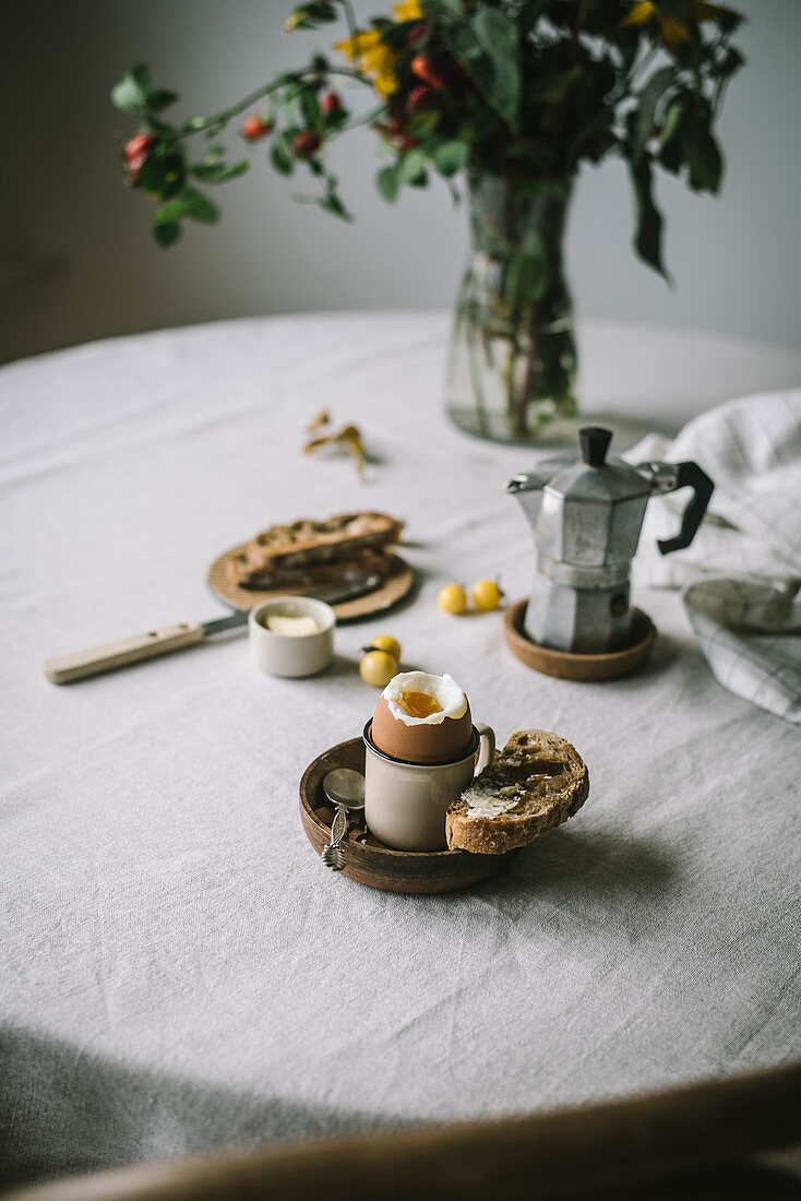 Gekochtes Ei, Brot und Espressokanne auf Frühstückstisch