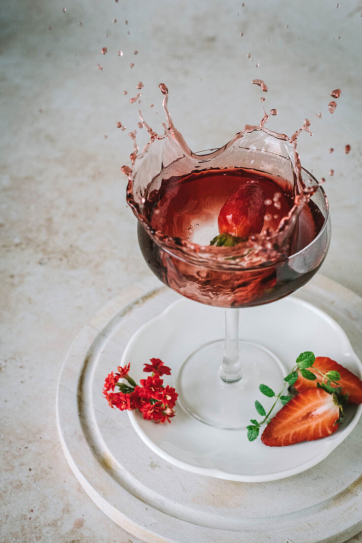 Erdbeere fällt spritzend in Rotweinglas