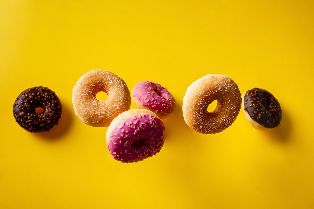 Various decorated doughnuts falling on yellow background