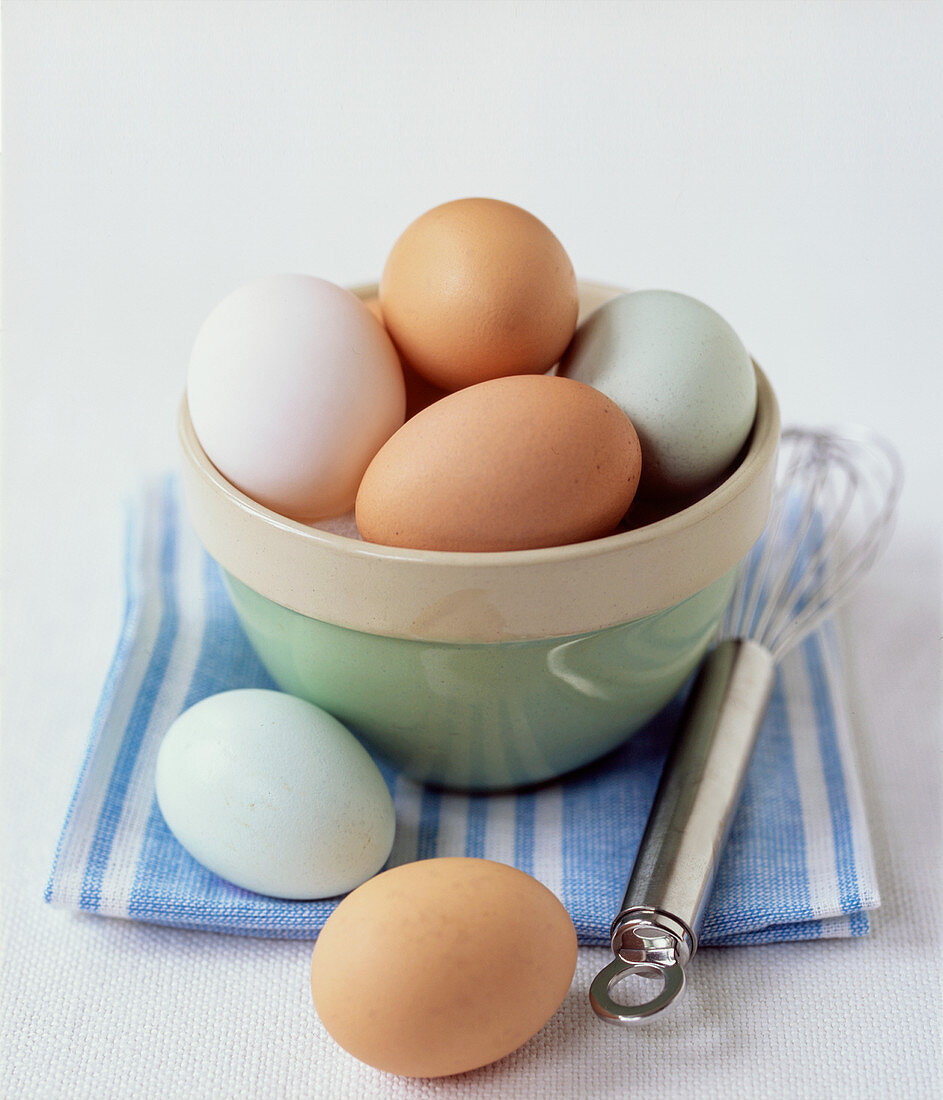 selection of different coloured organic eggs in a bowl with whisk