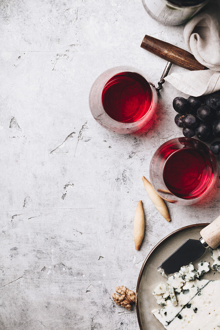 Zwei Gläser Rotwein, Käse und Trauben auf Steinuntergrund