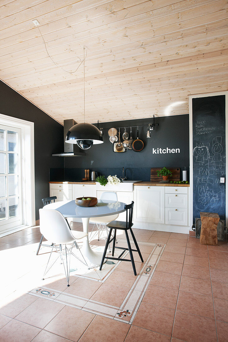 Frühstückstisch mit verschiedenen Stühlen vor weißer Einbauküche mit schwarzer Wand