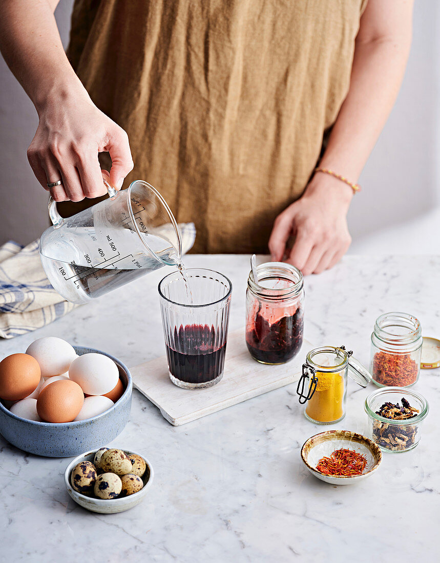 A person pours boiling water into a glass with blueberries