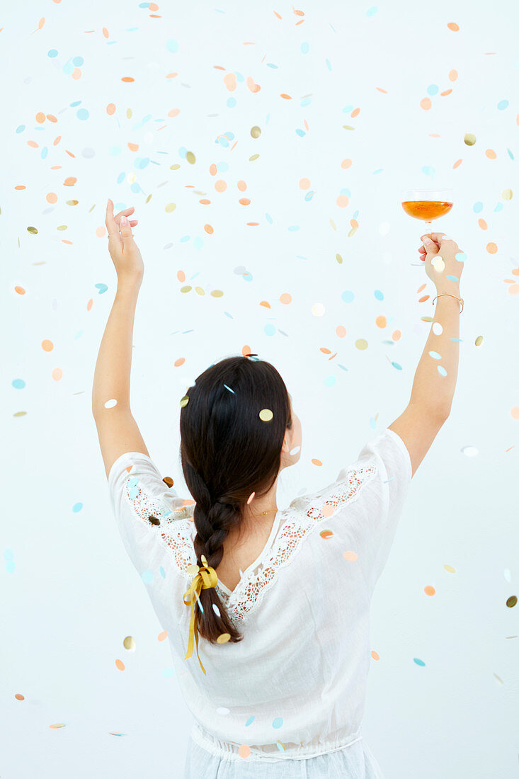 Young girl raises a cocktail under falling confetties