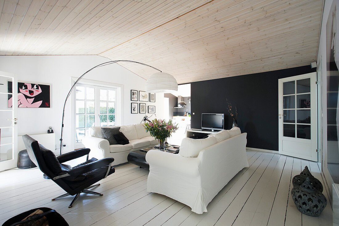 Loose-covered sofa and armchair next to arc lamp in black-and-white living room