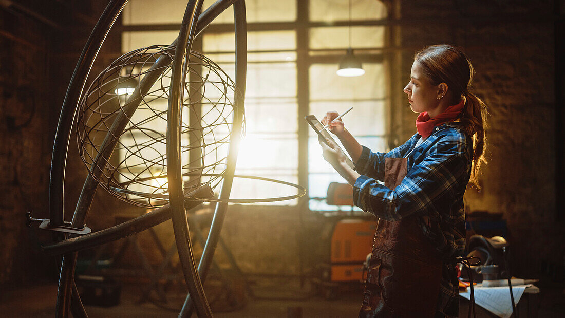 Sculptor sketching on a tablet next to a metal sculpture