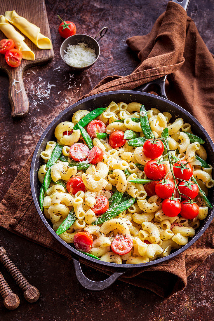 Pasta in cheese sauce with cherry tomatoes and sugar peas