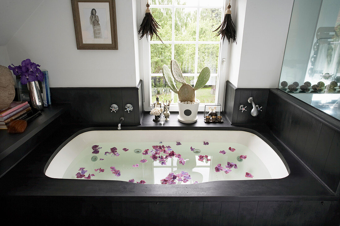 Rose petals floating in bathtub with black wooden surround