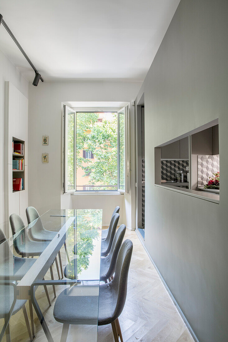 Glass table and chairs in a narrow dining room with gray walls and a serving window