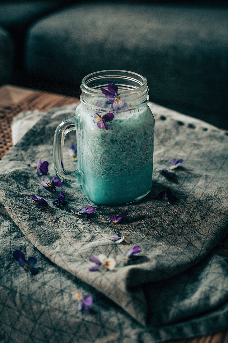Blauer Smoothie mit violetten Blüten im Henkelglas