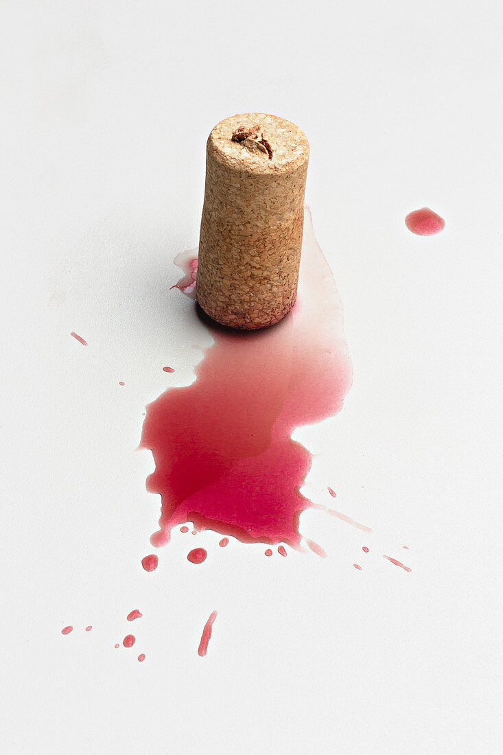 Cork and red wine splatter on white background