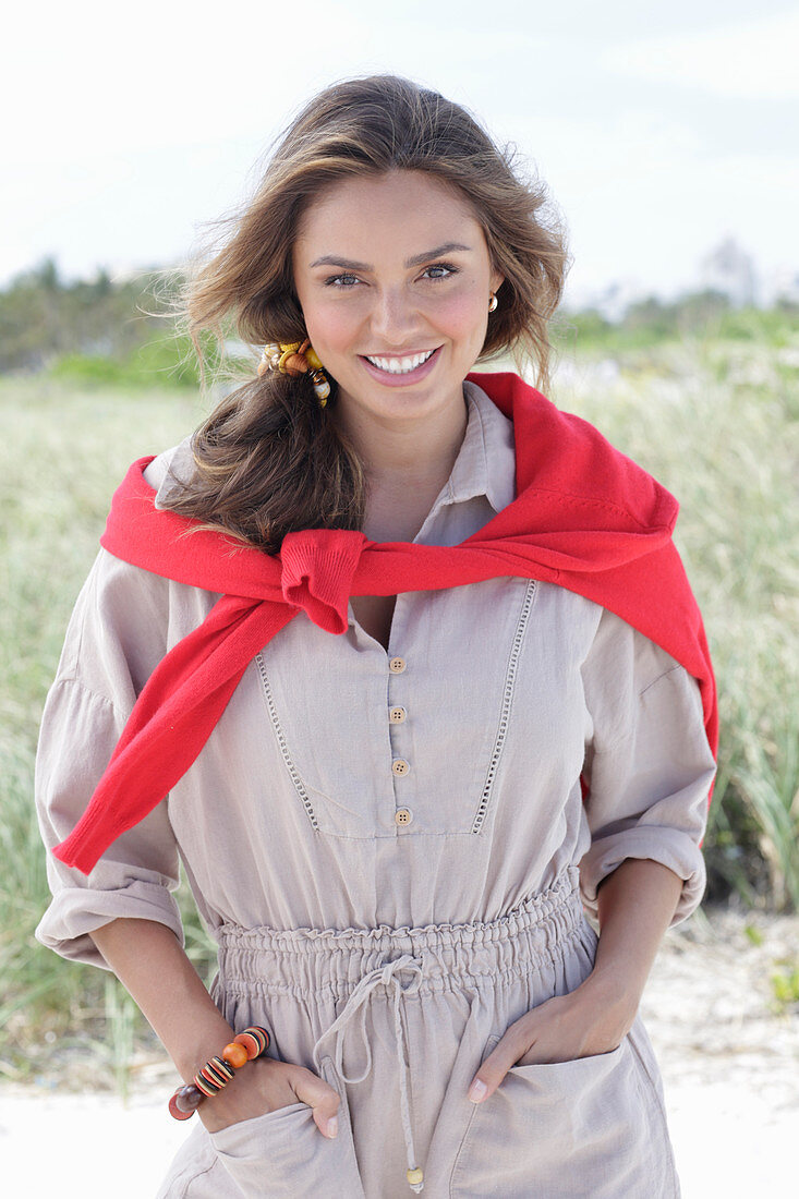 A young, long-haired woman wearing a beige linen blouse with a red jumper over her shoulder