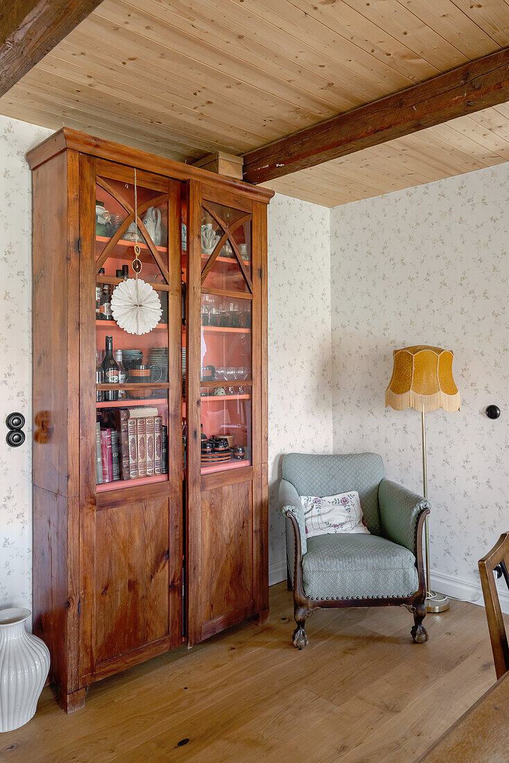 Glass-fronted cabinet, armchair and standard lamp in corner