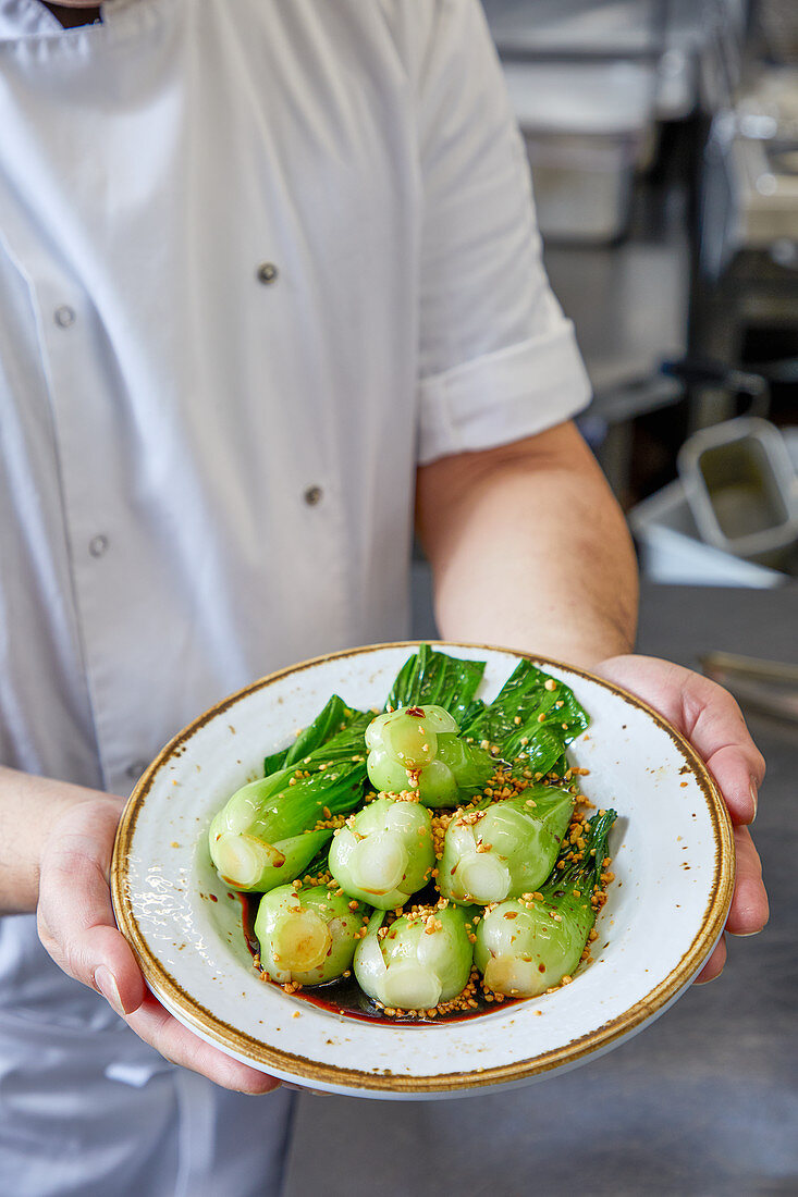 Koch serviert Pak Choi mit Knoblauch und Sojasauce