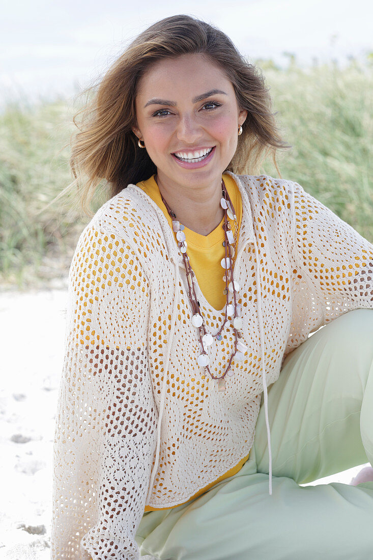 A young woman with long hair wearing a yellow t-shirt, a white crocheted jumper and trousers