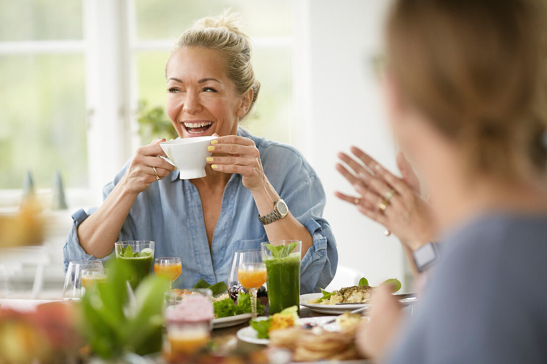 Lachende Frau mit Tasse am Tisch