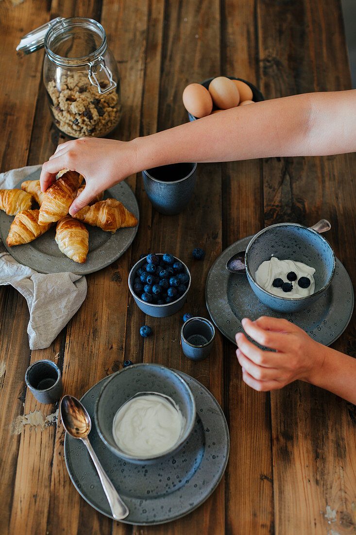 Hand greift nach Croissant am Frühstückstisch