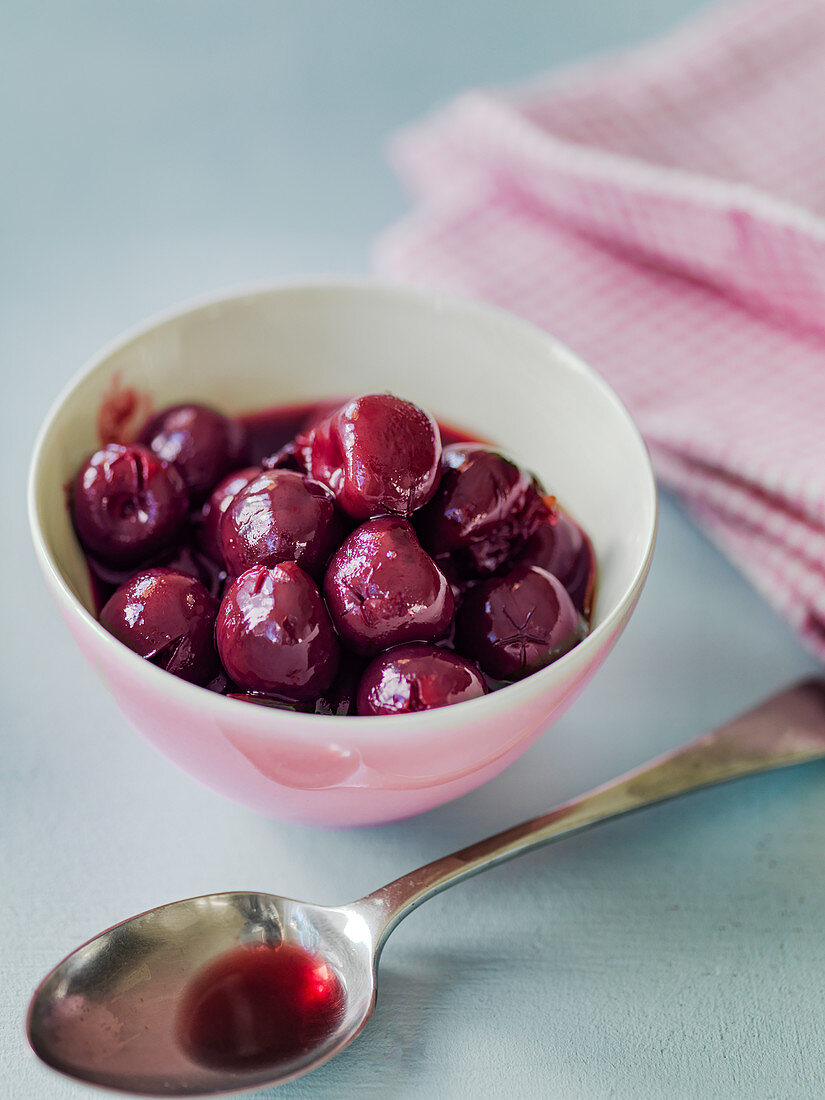 Cooked cherries in bowl with spoon showing juice