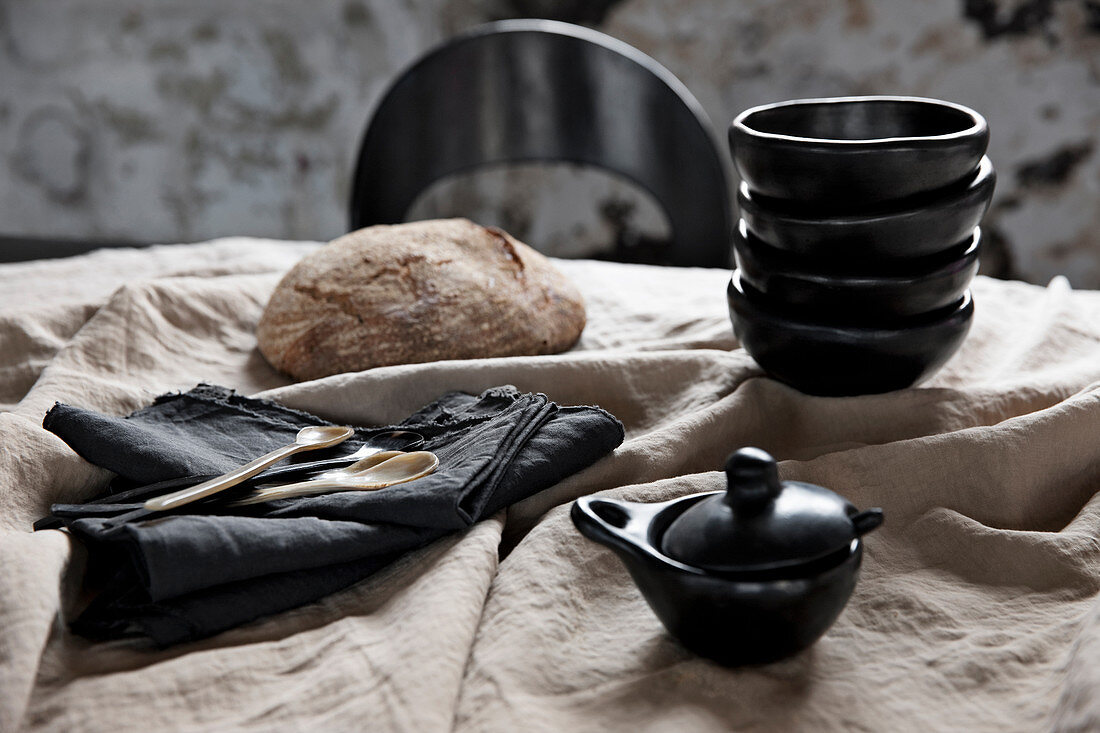 Schwarzes Geschirr, schwarze Servietten und Brot auf beiger Leinentischdecke