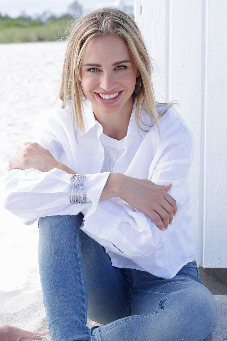 Blonde, langhaarige Frau in weißer Hemdbluse und Jeans