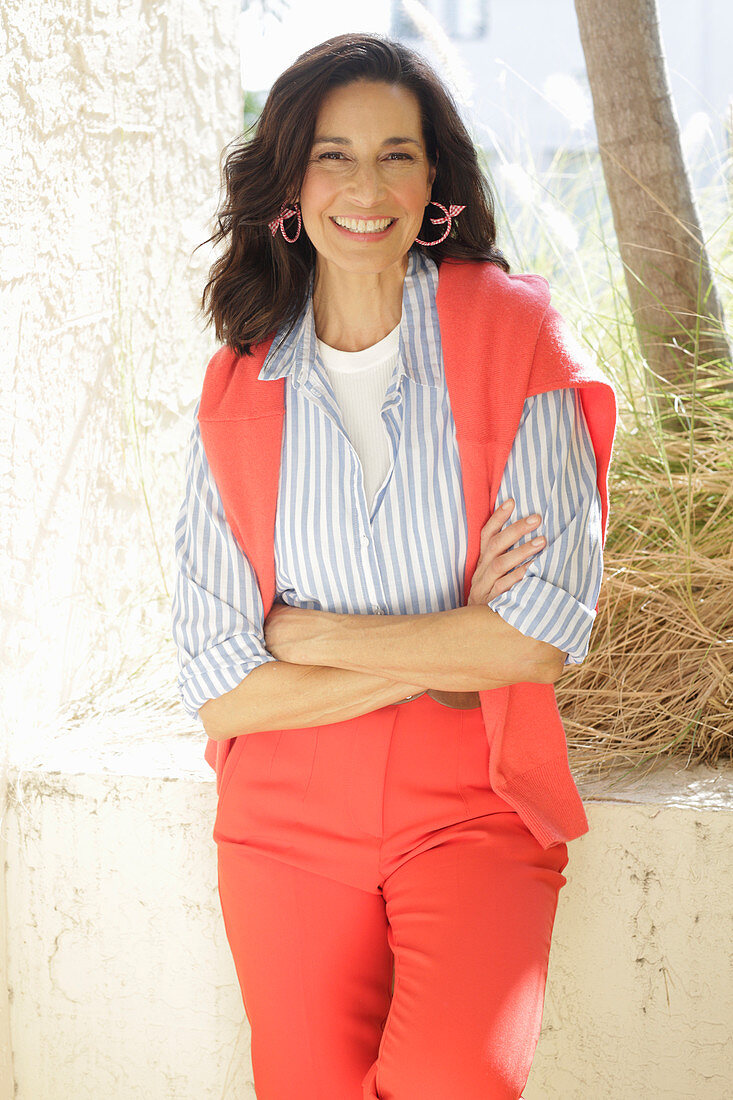 An older brunette woman wearing a blue-and-white striped shirt with a salmon-coloured jumper and trousers