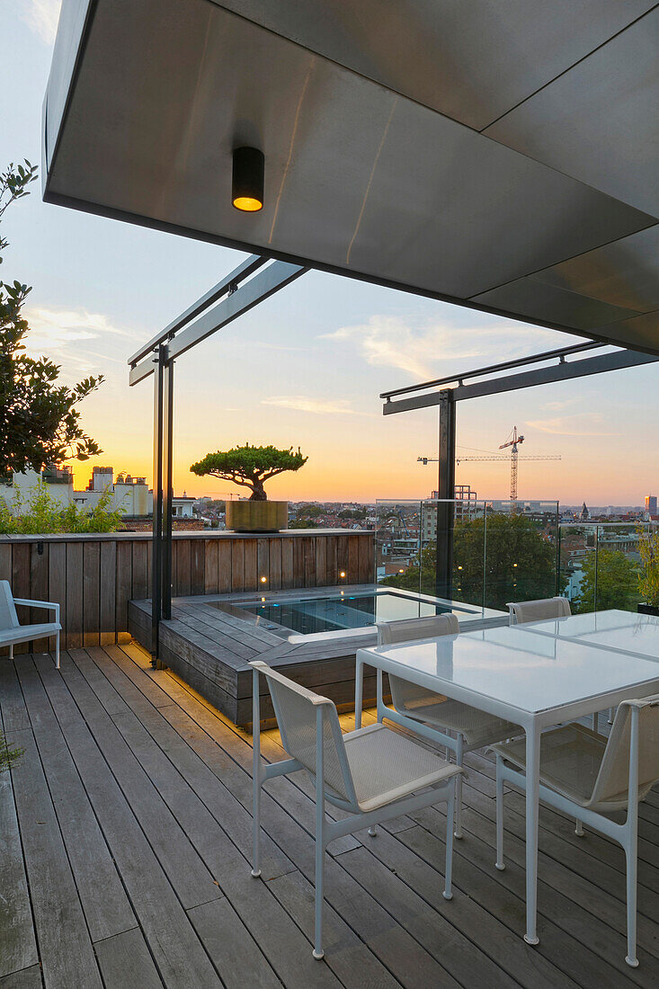 Holz-Dachterrasse mit Tisch, Stühlen und Pool beim Sonnenuntergang