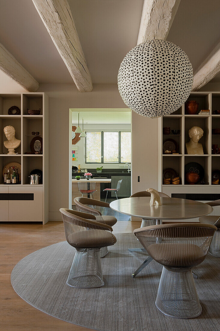 A dining area with designer chairs and a round table with a paper lampshade above